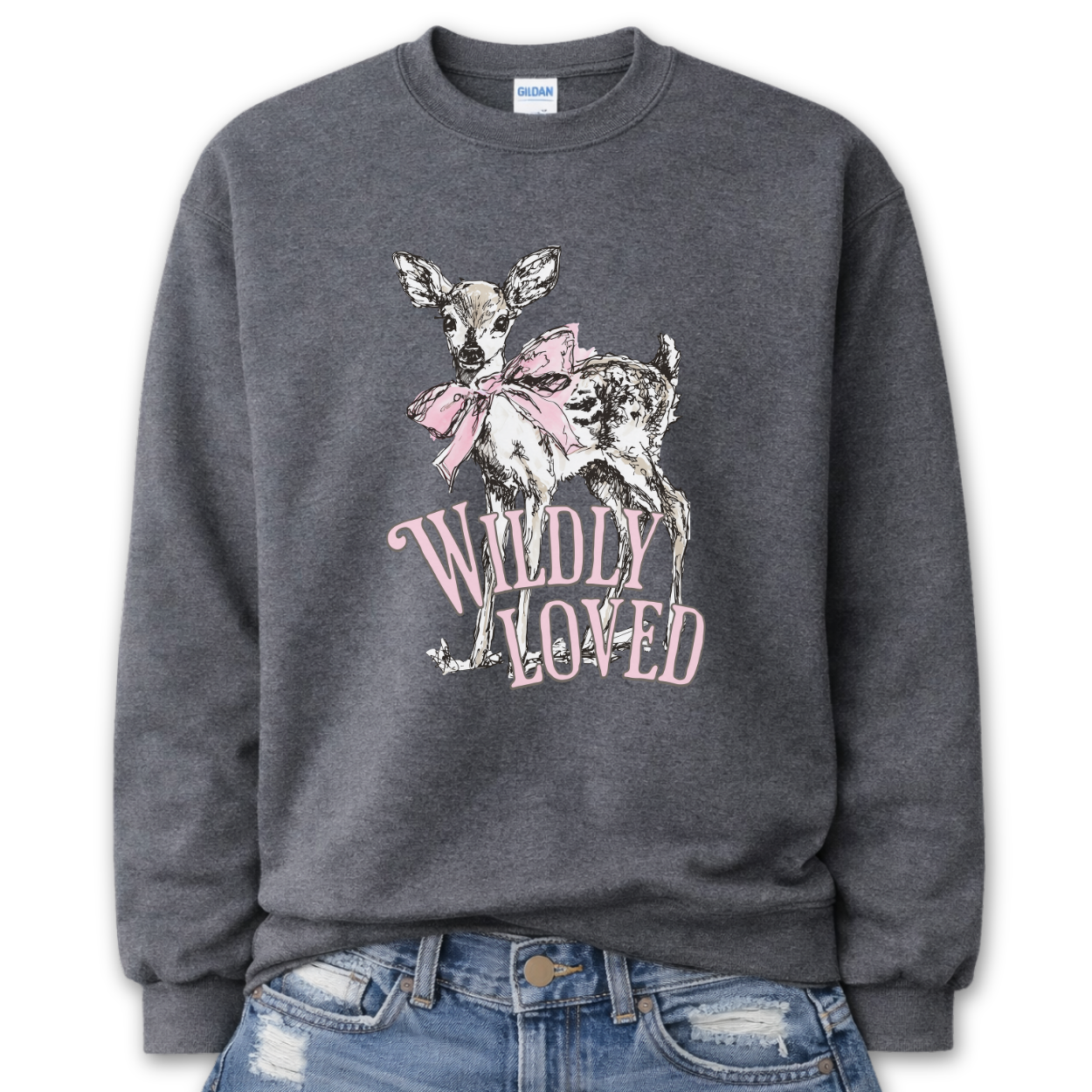 Dark Heather Gray Bold Christian graphic on a Gildan crewneck sweatshirt. The design features a fawn with soft brown detailing and a large pink bow, paired with the phrase “Wildly Loved” in blush vintage-style lettering. 