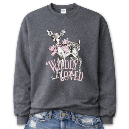 Dark Heather Gray Bold Christian graphic on a Gildan crewneck sweatshirt. The design features a fawn with soft brown detailing and a large pink bow, paired with the phrase “Wildly Loved” in blush vintage-style lettering. 
