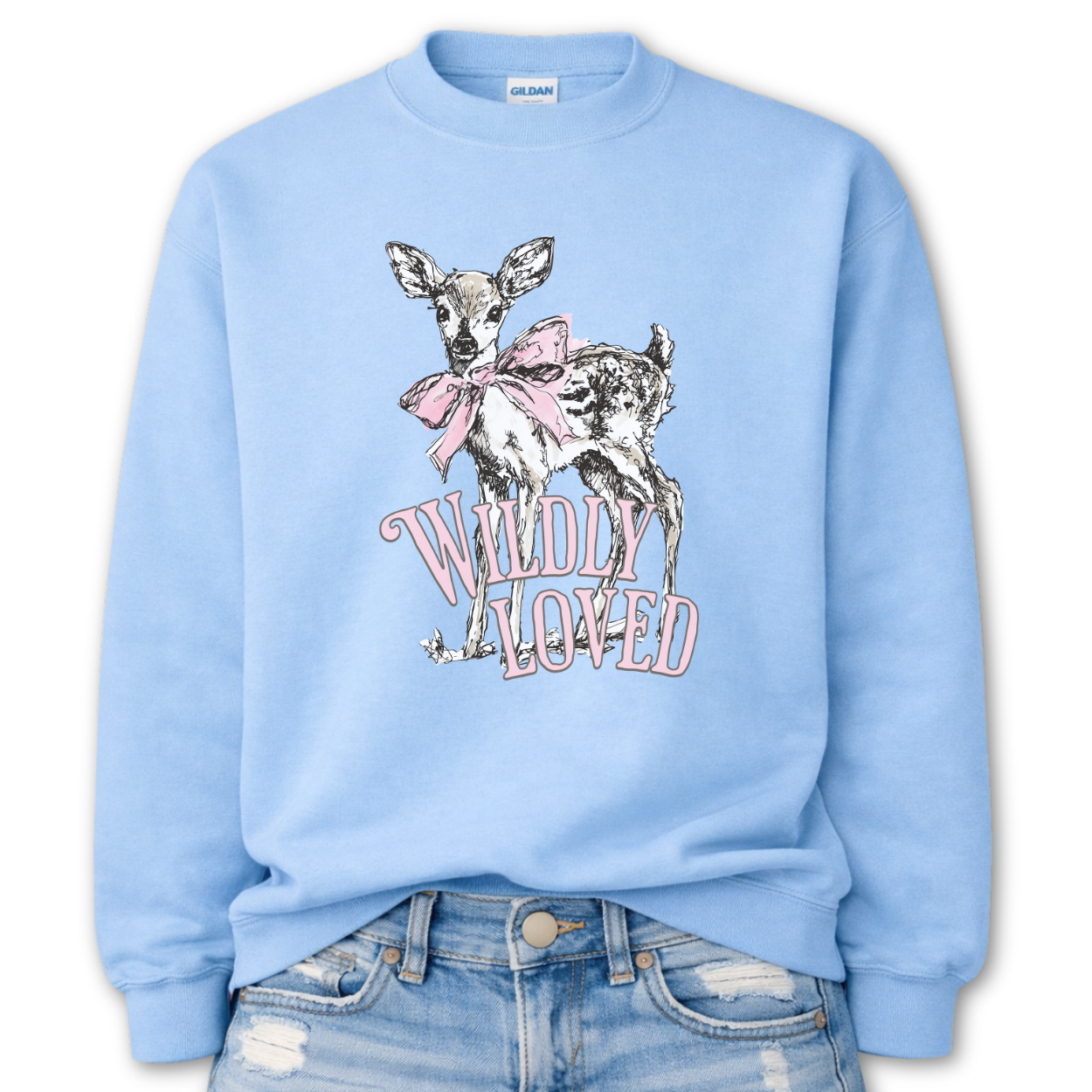 Blue Bold Christian graphic on a Gildan crewneck sweatshirt. The design features a fawn with soft brown detailing and a large pink bow, paired with the phrase “Wildly Loved” in blush vintage-style lettering. 