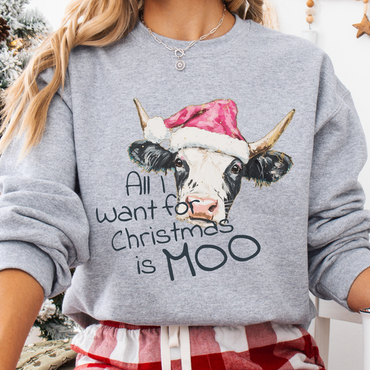 A woman wearing a heather gray crewneck sweatshirt with a graphic of a cow in a Santa hat and the text 'All I want for Christmas is MOO'.
