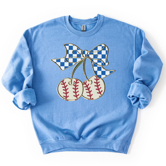 blue crewneck sweatshirt featuring a blue gingham bow tied to two cherry-shaped baseballs with red stitching, styled flat with sleeves scrunched