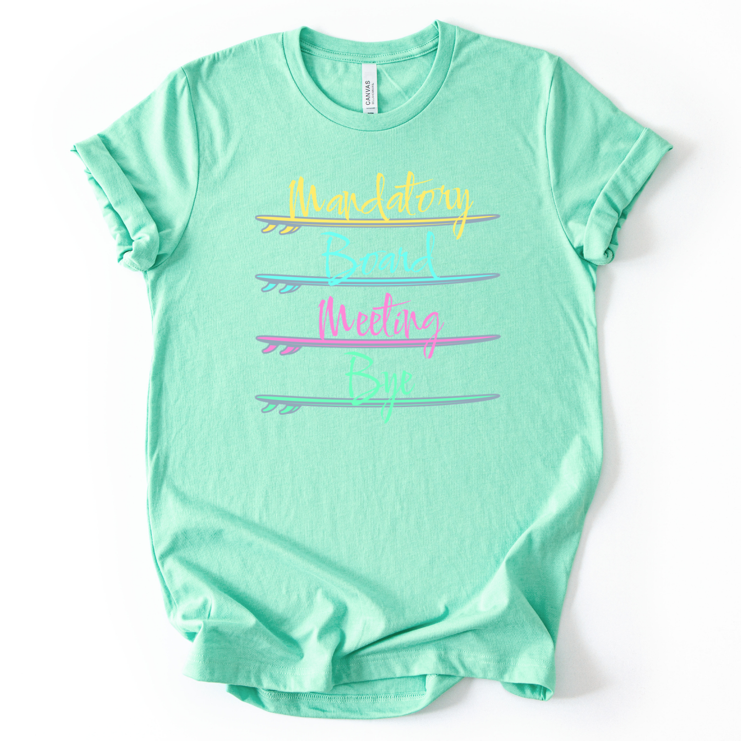 Surf themed beach graphic on a soft heather mint unisex graphic tee. The design features the phrase Mandatory Board Meeting Bye displayed across four stacked surfboards in bright summer colors including yellow, aqua, pink, and seafoam green. A lighthearted beach humor graphic that captures the feeling of skipping work for ocean time
