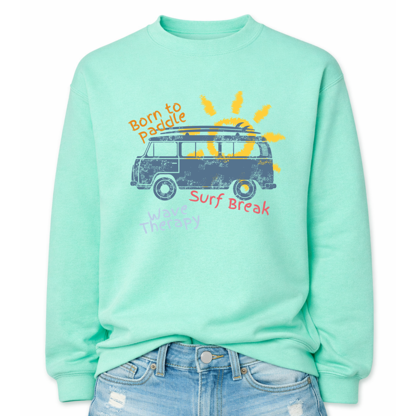Beach surf lifestyle graphic on a classic mint green crewneck sweatshirt. The design features a retro surf van with a surfboard mounted on the roof, set in front of a stylized sun graphic. The phrases Born To Paddle, Surf Break, and Wave Therapy surround the van illustration, creating a layered beach adventure layout inspired by surf culture and coastal travel.