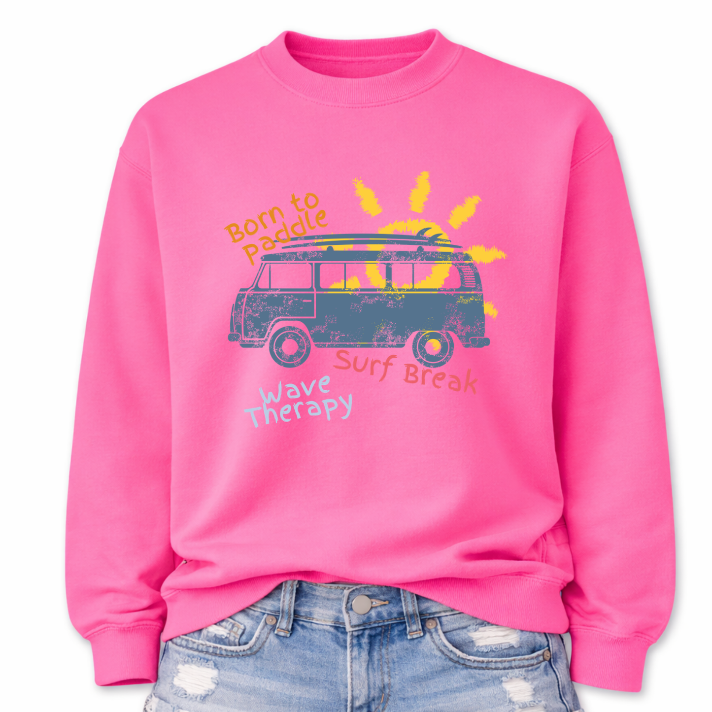  Beach surf lifestyle graphic on a classic pink crewneck sweatshirt. The design features a retro surf van with a surfboard mounted on the roof, set in front of a stylized sun graphic. The phrases Born To Paddle, Surf Break, and Wave Therapy surround the van illustration, creating a layered beach adventure layout inspired by surf culture and coastal travel.