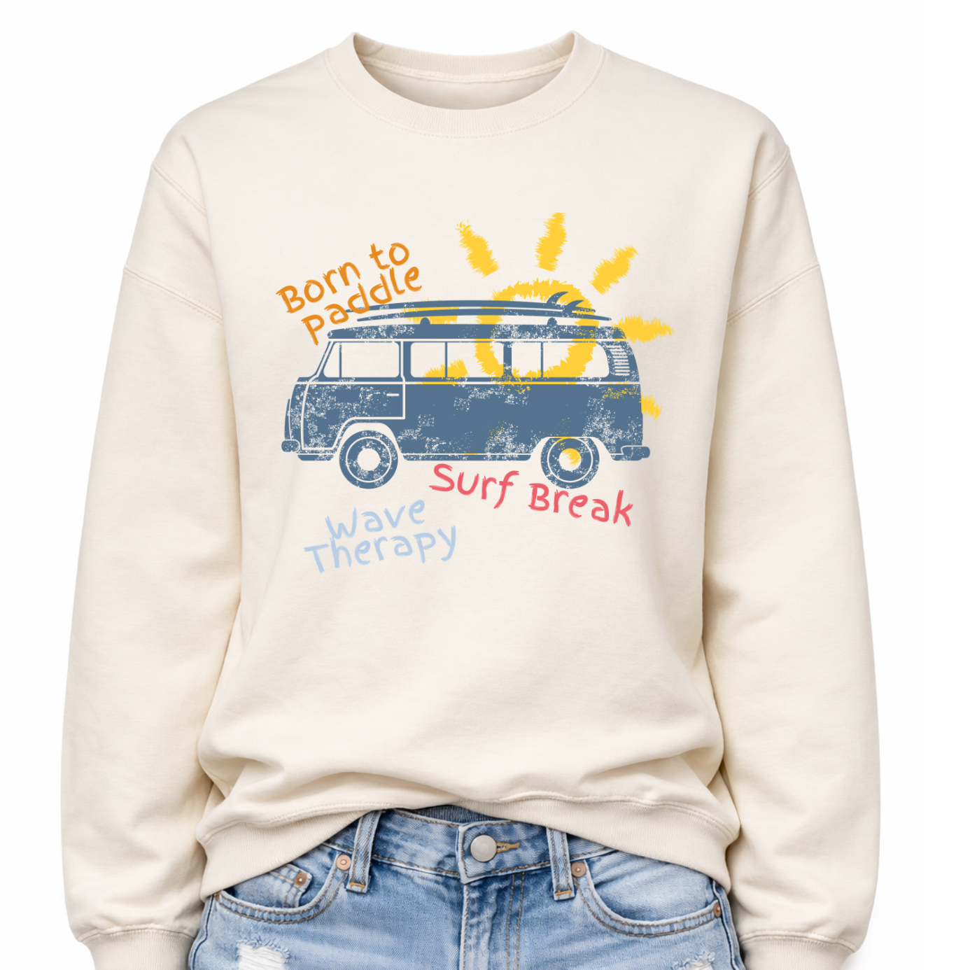 Beach surf lifestyle graphic on a classic off white crewneck sweatshirt. The design features a retro surf van with a surfboard mounted on the roof, set in front of a stylized sun graphic. The phrases Born To Paddle, Surf Break, and Wave Therapy surround the van illustration, creating a layered beach adventure layout inspired by surf culture and coastal travel.