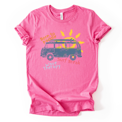 Summer beach graphic on a soft unisex heather charity pink graphic tee. The design features a vintage surf van illustration with a surfboard on top and a bright sun rising behind the vehicle. Playful coastal phrases including Born to Paddle, Surf Break, and Wave Therapy surround the artwork, creating a relaxed surf and beach lifestyle graphic that captures the feeling of ocean days and summer travel.