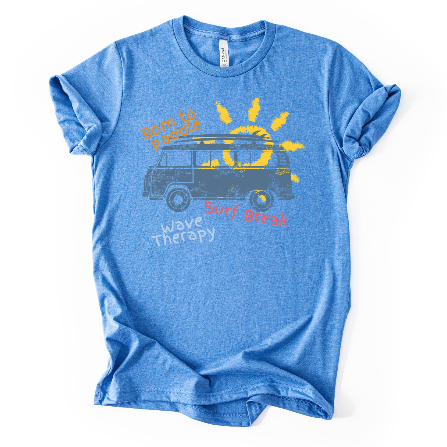 Summer beach graphic on a soft unisex heather carolina blue graphic tee. The design features a vintage surf van illustration with a surfboard on top and a bright sun rising behind the vehicle. Playful coastal phrases including Born to Paddle, Surf Break, and Wave Therapy surround the artwork, creating a relaxed surf and beach lifestyle graphic that captures the feeling of ocean days and summer travel.