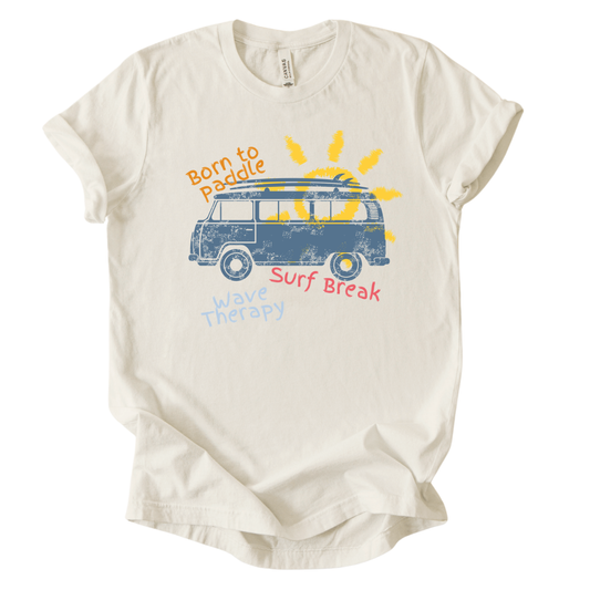 Summer beach graphic on a soft unisex heather oatmeal graphic tee. The design features a vintage surf van illustration with a surfboard on top and a bright sun rising behind the vehicle. Playful coastal phrases including Born to Paddle, Surf Break, and Wave Therapy surround the artwork, creating a relaxed surf and beach lifestyle graphic that captures the feeling of ocean days and summer travel.