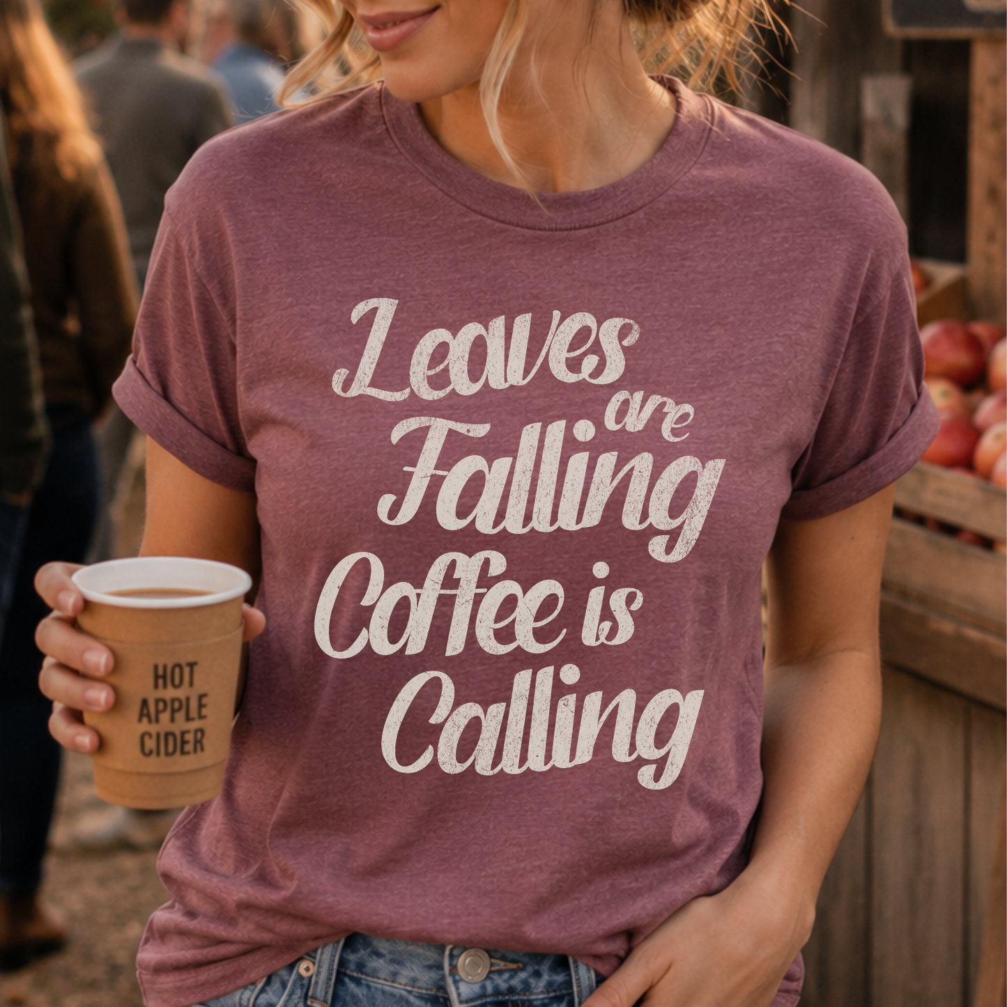 Person wearing a purple t-shirt with 'Leaves are falling, coffee is calling' text, holding a cup of hot apple cider.