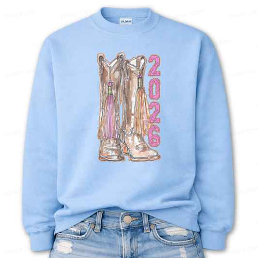 Light blue sweatshirt with cowboy boots and '2026' printed on it, worn with distressed jeans.