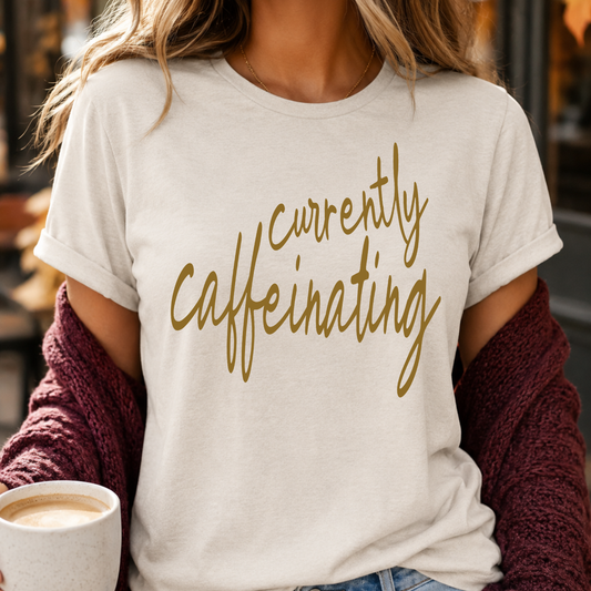 Person wearing a white t-shirt with 'currently caffeinating' text, holding a coffee cup.