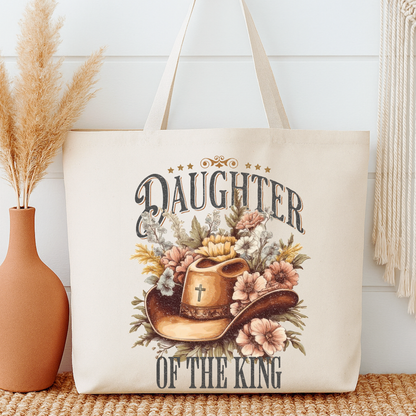 Tote bag with 'Daughter of the King' design featuring a cowboy hat and flowers, placed on a surface with a vase and decorative items.