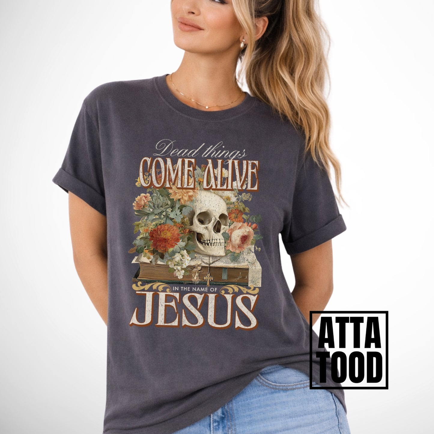 Dead things come alive in the name of Jesus with an oversized graphic of a bible, skeleton head and flowers on a comfort colors pepper gray tee
