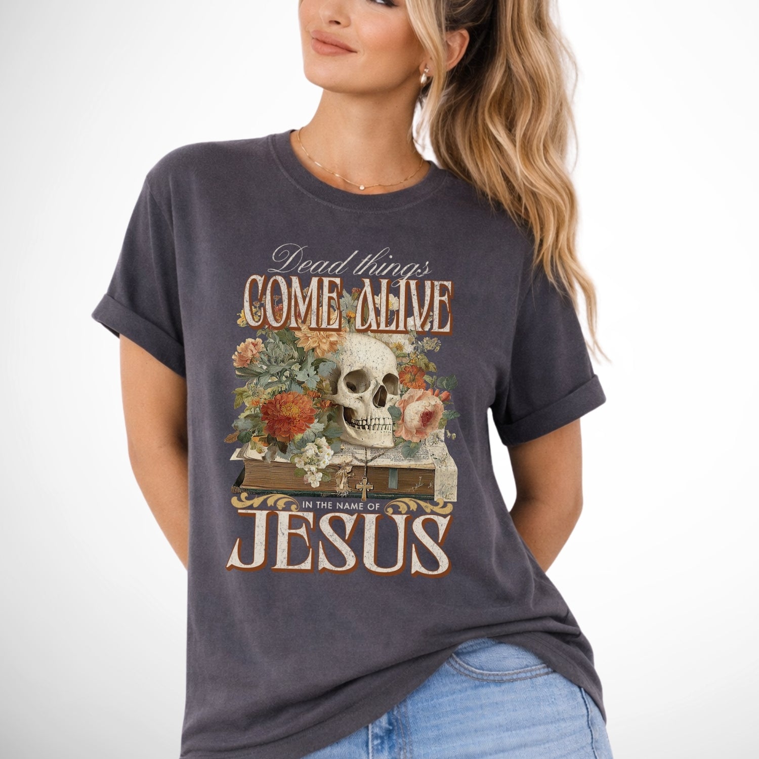 Dead things come alive in the name of Jesus with an oversized graphic of a bible, skeleton head and flowers on a comfort colors pepper gray tee