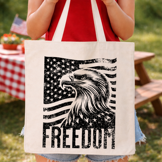 Patriotic Fourth of July historical graphic on a 100% cotton canvas tote bag. The design features bold oversized “1776” typography centered on the bag, layered with “Philadelphia July 4th” text above and “The Dawn of American Freedom” below in distressed red, white, and blue lettering for a classic Americana, history-forward look ideal for Independence Day merchandising.