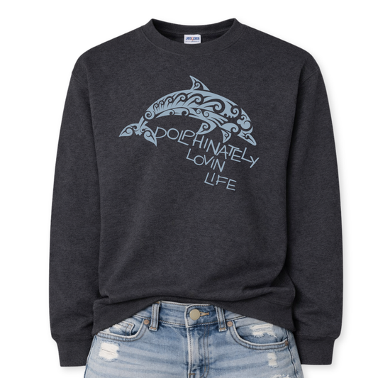 Coastal ocean graphic on a classic ivory heather black crewneck sweatshirt. The design features a large dolphin illustration filled with decorative swirl and wave inspired pattern details that give the sea life artwork a textured ocean aesthetic. The phrase Dolphinately Lovin Life is integrated into the graphic beneath the dolphin.