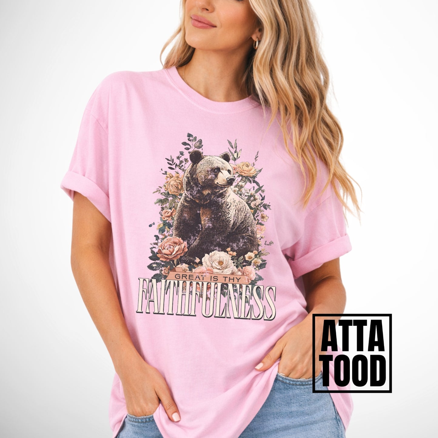 Woman wearing a pink t-shirt with a bear and floral design, text 'Great is thy Faithfulness', and 'ATTA TOOD' branding.
