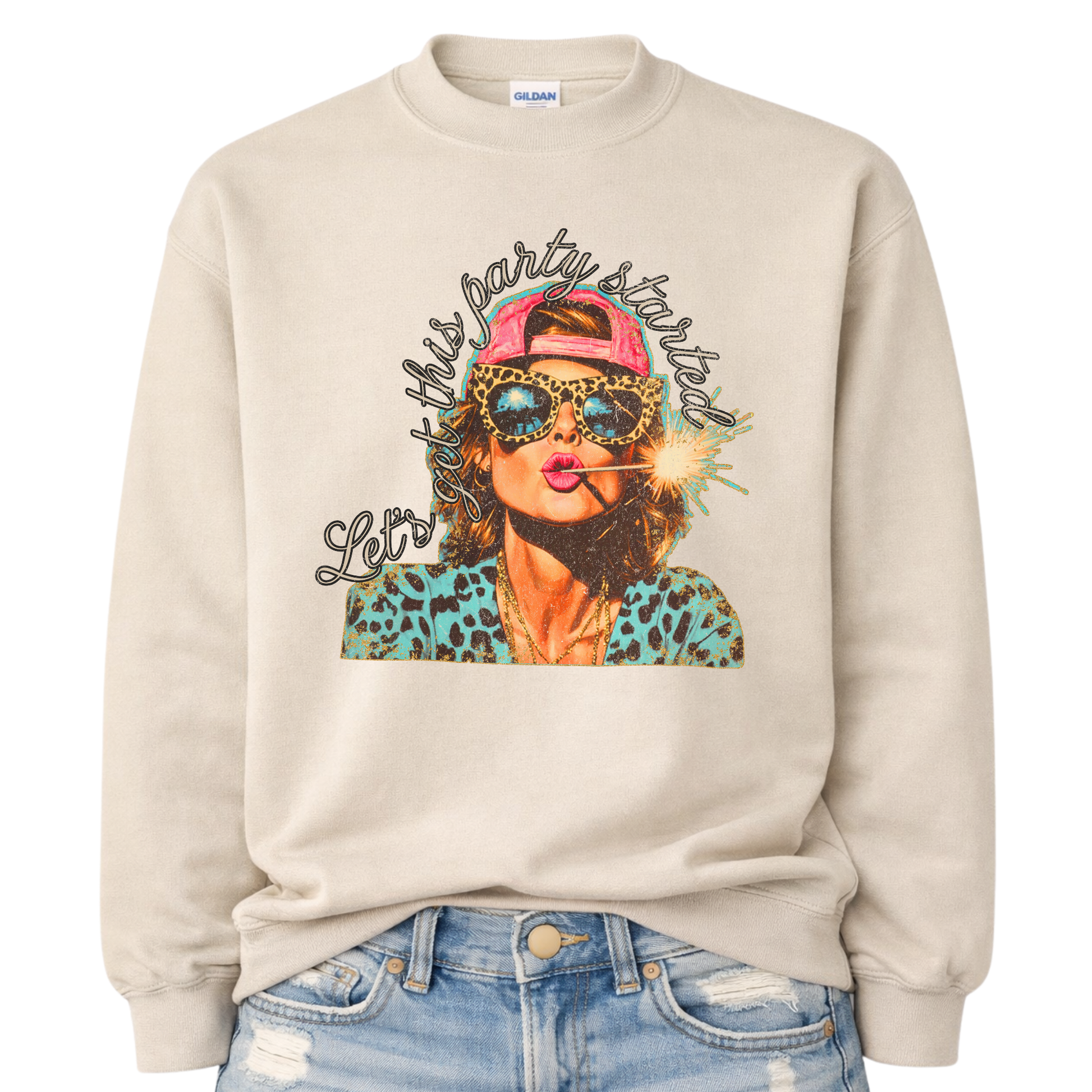 Patriotic Fourth of July graphic on a beige sweatshirt. The design features an illustrated woman wearing leopard-print sunglasses and a backward cap, holding a lit sparkler in her mouth. The artwork is layered with bold color contrasts, distressed textures, and playful script lettering that reads “Let’s Get This Party Started.” A high-energy patriotic design blending Americana attitude with modern pop-art style