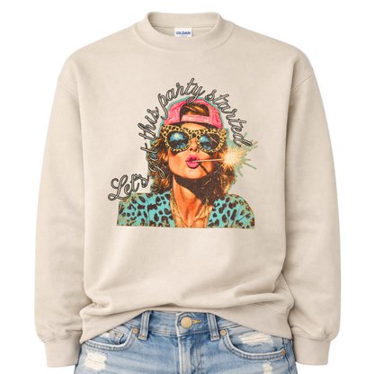 Patriotic Fourth of July graphic on a beige sweatshirt. The design features an illustrated woman wearing leopard-print sunglasses and a backward cap, holding a lit sparkler in her mouth. The artwork is layered with bold color contrasts, distressed textures, and playful script lettering that reads “Let’s Get This Party Started.” A high-energy patriotic design blending Americana attitude with modern pop-art style