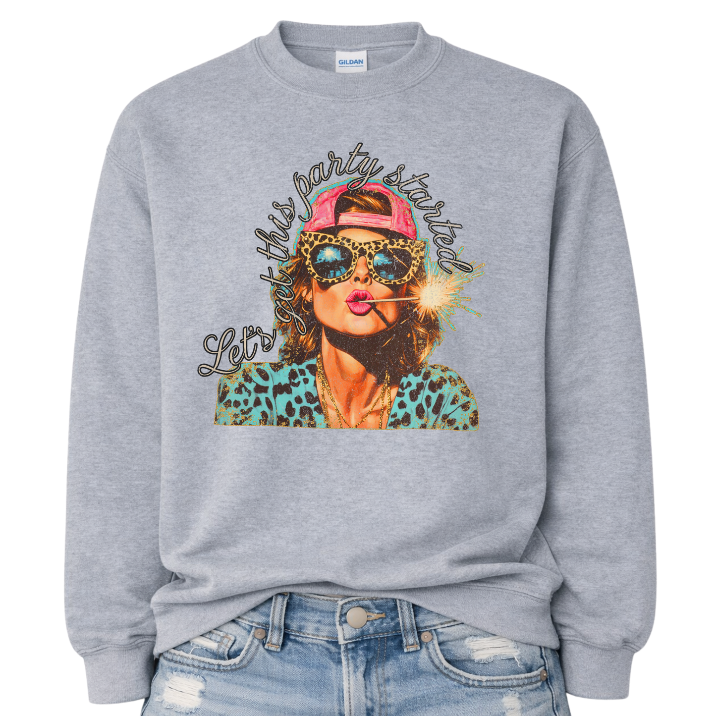 Patriotic Fourth of July graphic on a sport gray sweatshirt. The design features an illustrated woman wearing leopard-print sunglasses and a backward cap, holding a lit sparkler in her mouth. The artwork is layered with bold color contrasts, distressed textures, and playful script lettering that reads “Let’s Get This Party Started.” A high-energy patriotic design blending Americana attitude with modern pop-art style