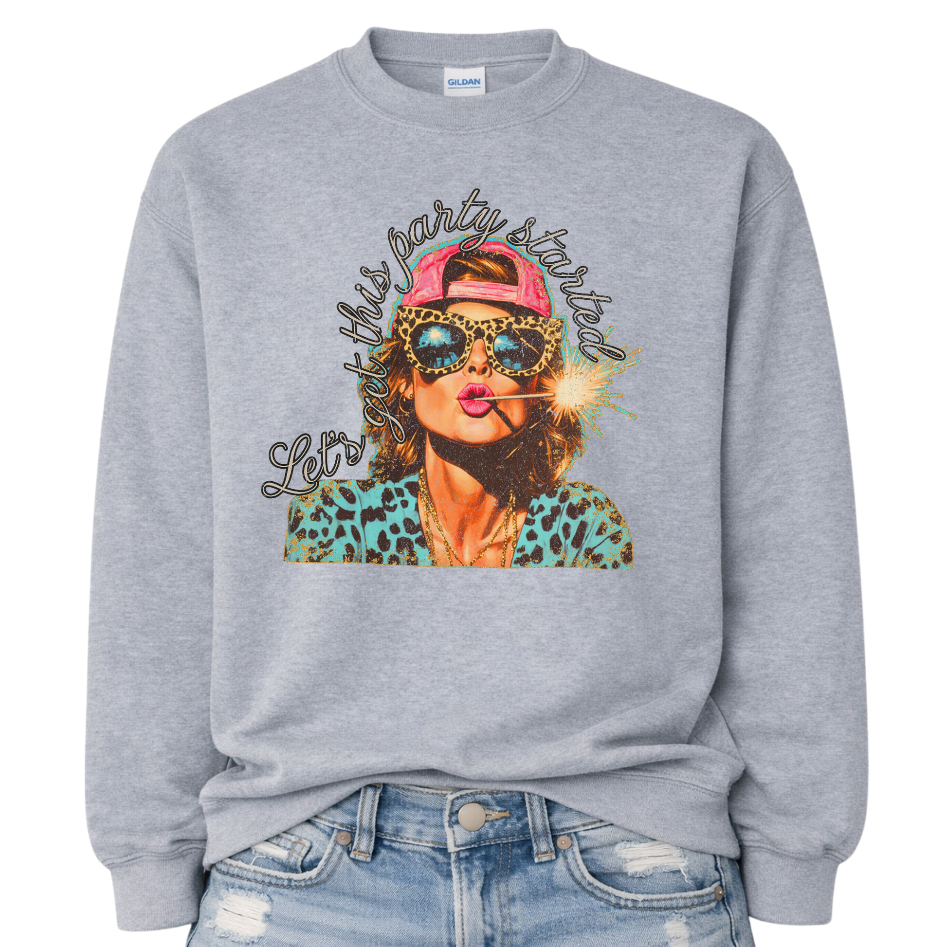 Patriotic Fourth of July graphic on a sport gray sweatshirt. The design features an illustrated woman wearing leopard-print sunglasses and a backward cap, holding a lit sparkler in her mouth. The artwork is layered with bold color contrasts, distressed textures, and playful script lettering that reads “Let’s Get This Party Started.” A high-energy patriotic design blending Americana attitude with modern pop-art style
