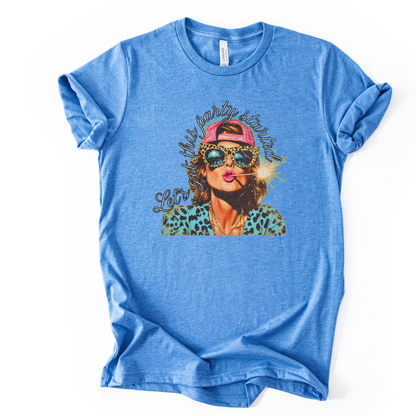 blue Patriotic Fourth of July graphic on a white  t-shirt. The design features an illustrated woman wearing leopard-print sunglasses and a backward cap, holding a lit sparkler with fireworks reflected in the lenses. Curved script lettering adds a playful party vibe, blending bold Americana colors with a modern, fun-forward patriotic style ideal for summer celebrations.
