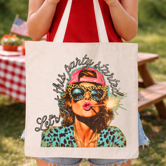 Patriotic Fourth of July party-themed graphic on a 100% cotton canvas tote bag. The design features a bold illustrated woman wearing a backward cap and sunglasses, blowing a sparkler with playful “Let’s Get the Party Started” script, layered in bright red, blue, and leopard-print accents for a fun, modern Americana look.
