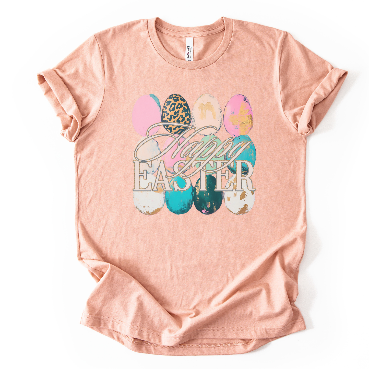 A peach graphic t-shirt printed on a Bella Canvas® premium retail-fit tee.

The graphic features a row of illustrated Easter eggs in varied shapes and sizes, decorated with mixed patterns including leopard print, soft pastels, abstract brush textures, and distressed accents. The phrase “Happy Easter” overlays the eggs in elegant script and block lettering,