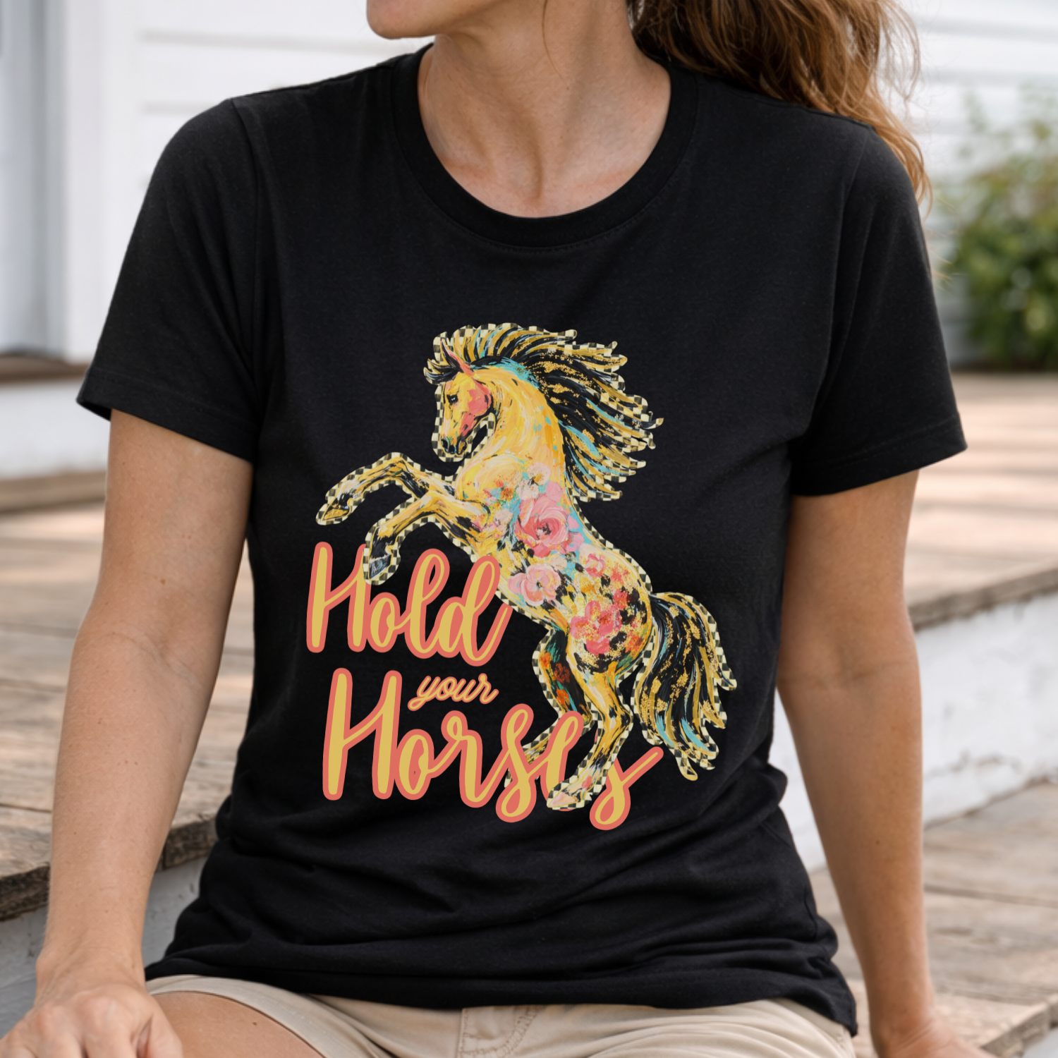 Person wearing a black t-shirt with a colorful horse graphic and 'Hold your Horses' text.