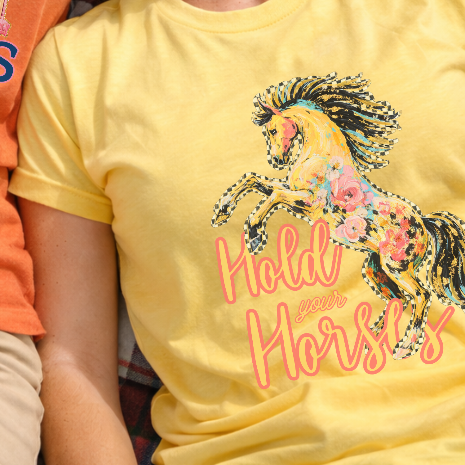 Person wearing a yellow t-shirt with a horse graphic and text, sitting next to an orange t-shirt with a barn design.