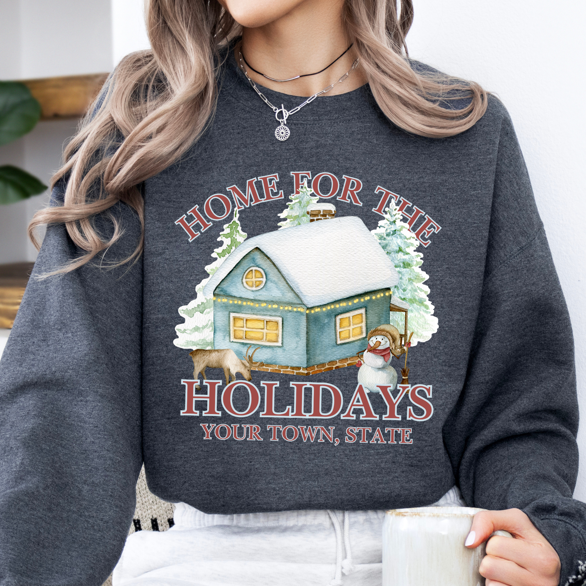 Home for the holidays dark gray sweatshirt with graphics of a home in the snow, trees, snowman and a deer.  customize with business name, city and state or both