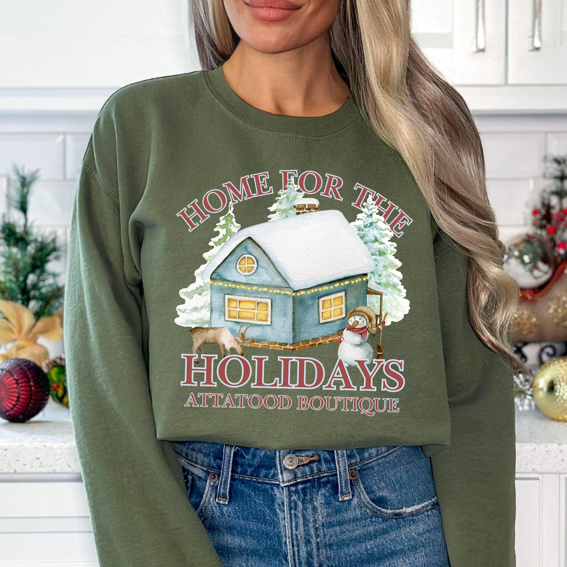 Home for the holidays military green sweatshirt with graphics of a home in the snow, trees, snowman and a deer.  customize with business name, city and state or both