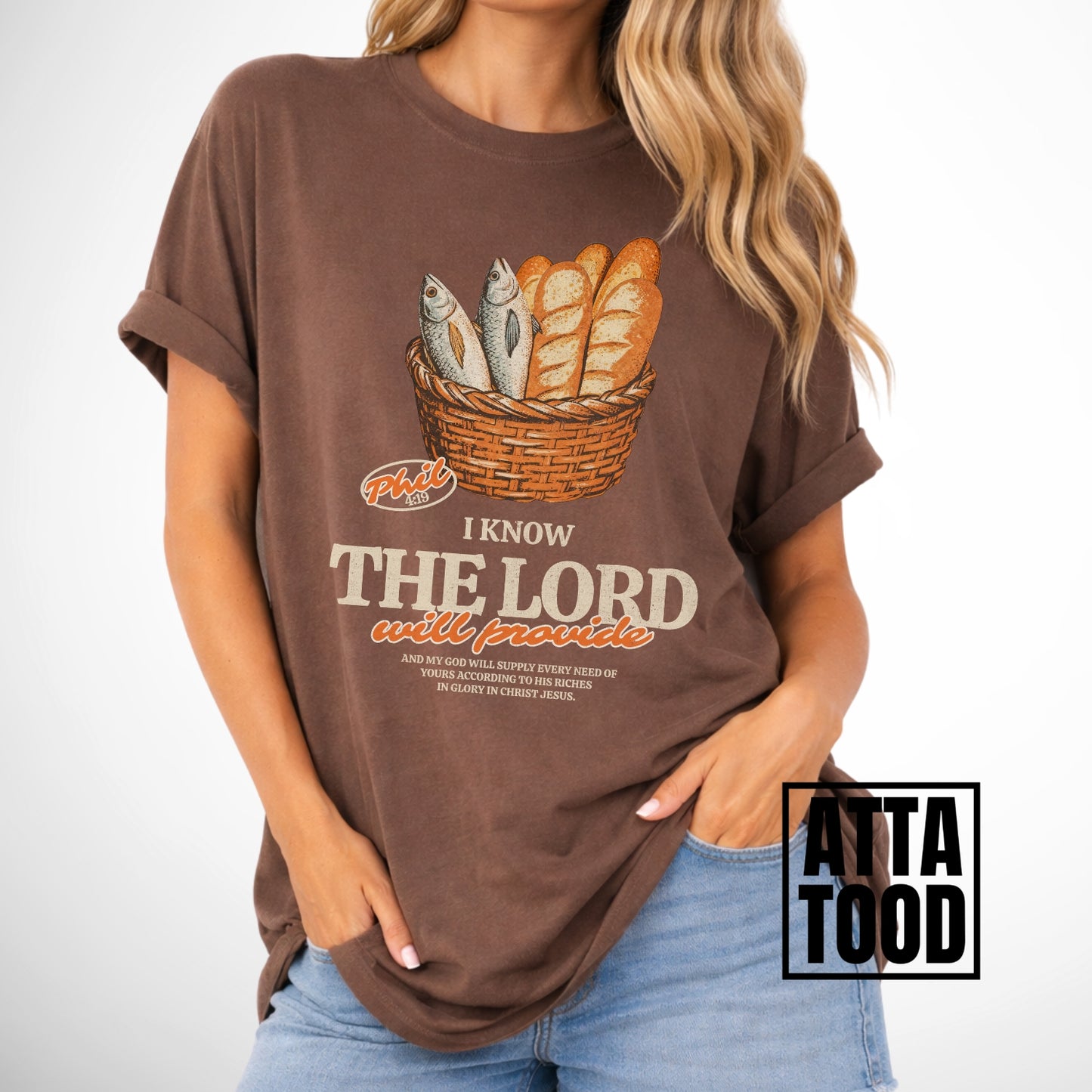Person wearing a brown t-shirt with a graphic design and text.  I know the Lord will provide featuring a basket of bread and fish referencing bible verse Philipians 4:19