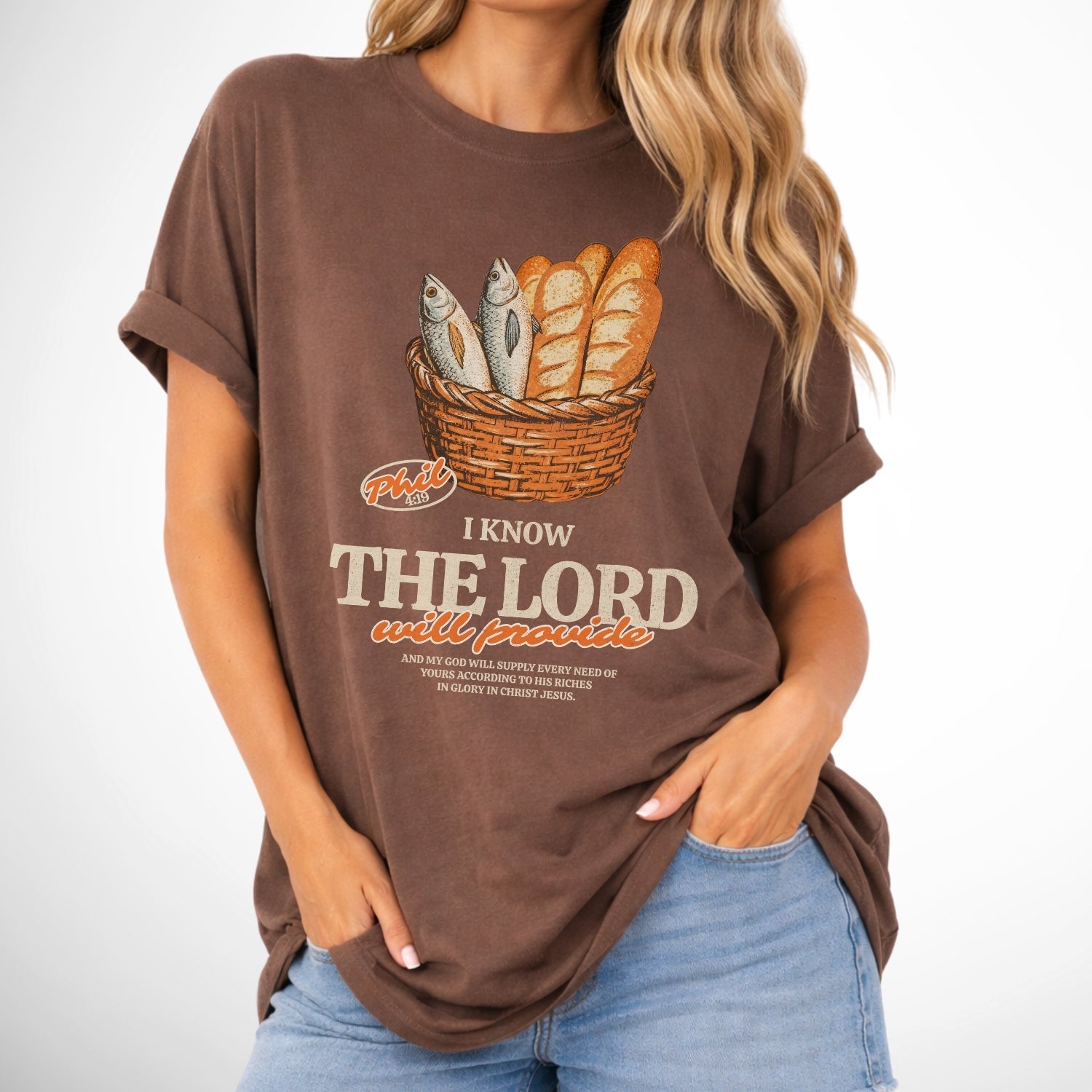 Person wearing a brown t-shirt with a graphic and text on a white background. I know the Lord will provide featuring a basket of bread and fish referencing bible verse Philipians 4:19