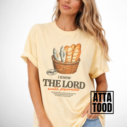 Person wearing a yellow t-shirt with a graphic design and text.  I know the Lord will provide featuring a basket of bread and fish referencing bible verse Philipians 4:19