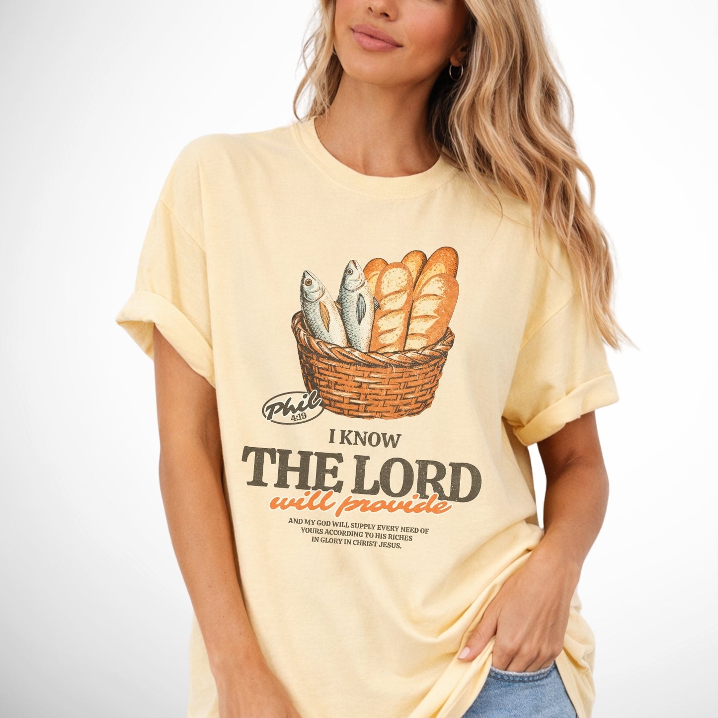 Woman wearing a yellow t-shirt with a basket graphic and text. I know the Lord will provide featuring a basket of bread and fish referencing bible verse Philipians 4:19