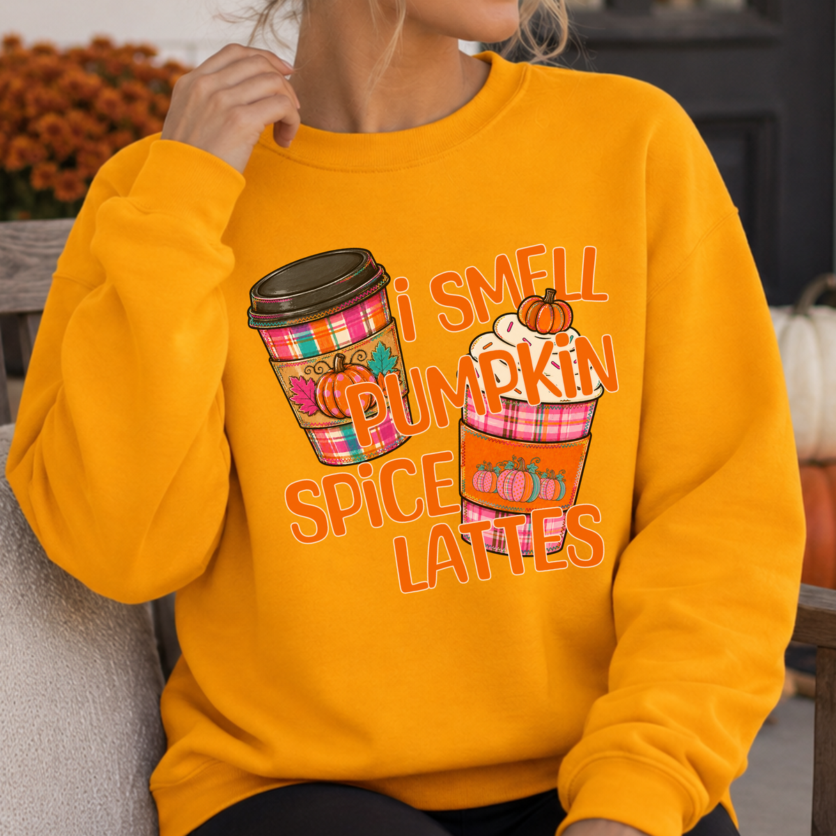 I smell pumpkin spice lattes featuring two coffee cups in fall plaid bright colors, orange, pink and teal with pumpkins on the sleeves of the cup warmers.  Gold sweatshirt