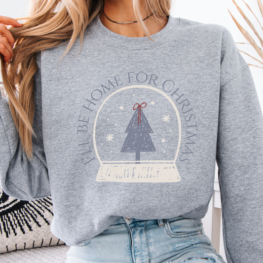 A sweet holiday graphic featuring a hand-drawn snow globe, Christmas tree, and the saying “I’ll Be Home for Christmas.” on ash gray sweatshirt