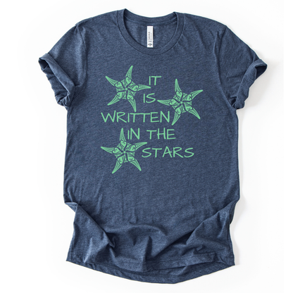 Coastal beach graphic on a soft unisex heather navy graphic tee. The design features the phrase It Is Written In The Stars surrounded by illustrated sea stars. The starfish artwork includes decorative coastal pattern details inside the shapes, giving the illustration a textured ocean inspired look. 