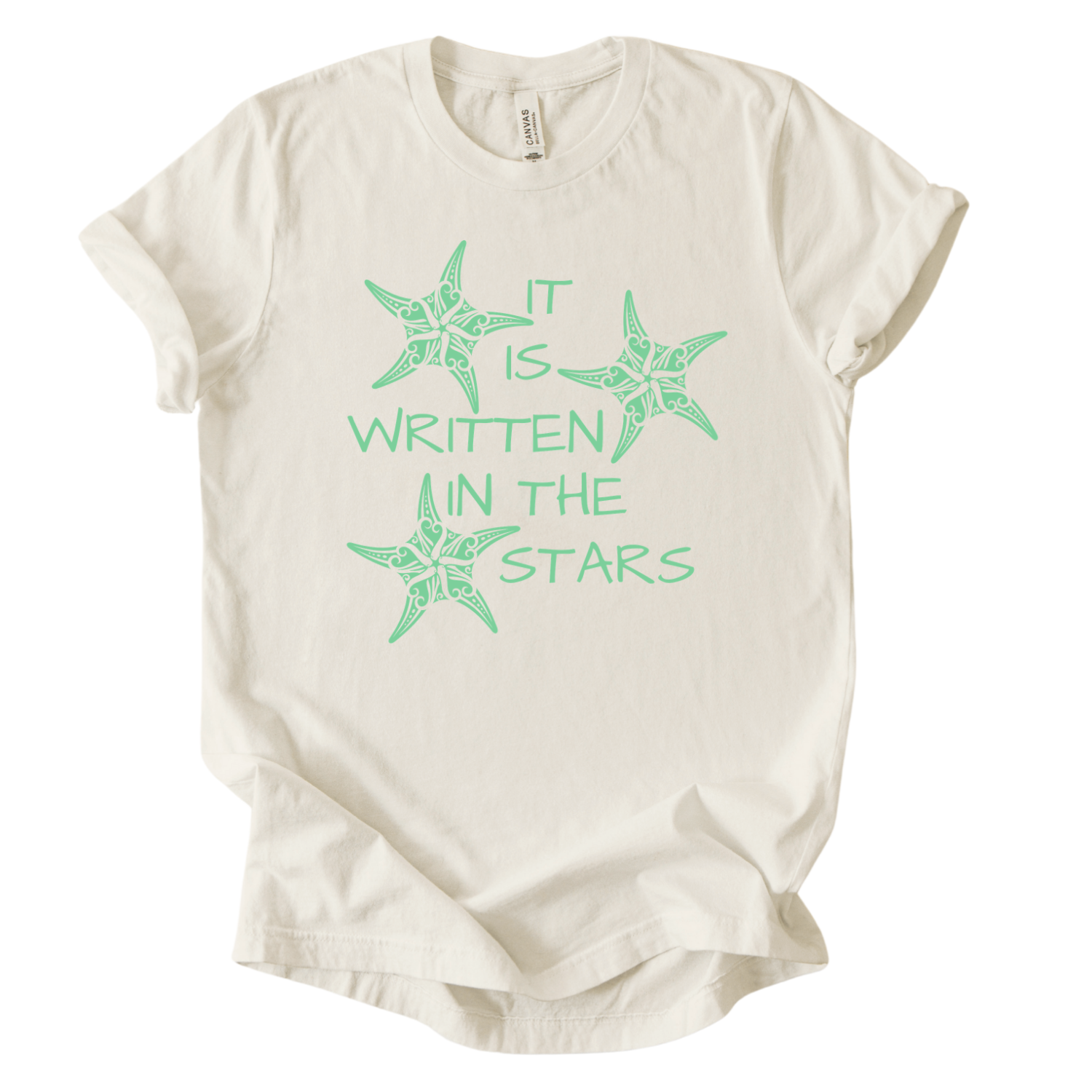 Coastal beach graphic on a soft unisex heather oatmeal graphic tee. The design features the phrase It Is Written In The Stars surrounded by illustrated sea stars. The starfish artwork includes decorative coastal pattern details inside the shapes, giving the illustration a textured ocean inspired look. 