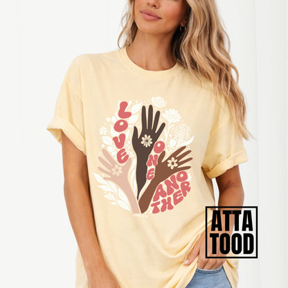 Person wearing a yellow t-shirt with a colorful graphic of hands and flowers on a white background. John 13 Love One Another Comfort Colors Graphic Tee 
