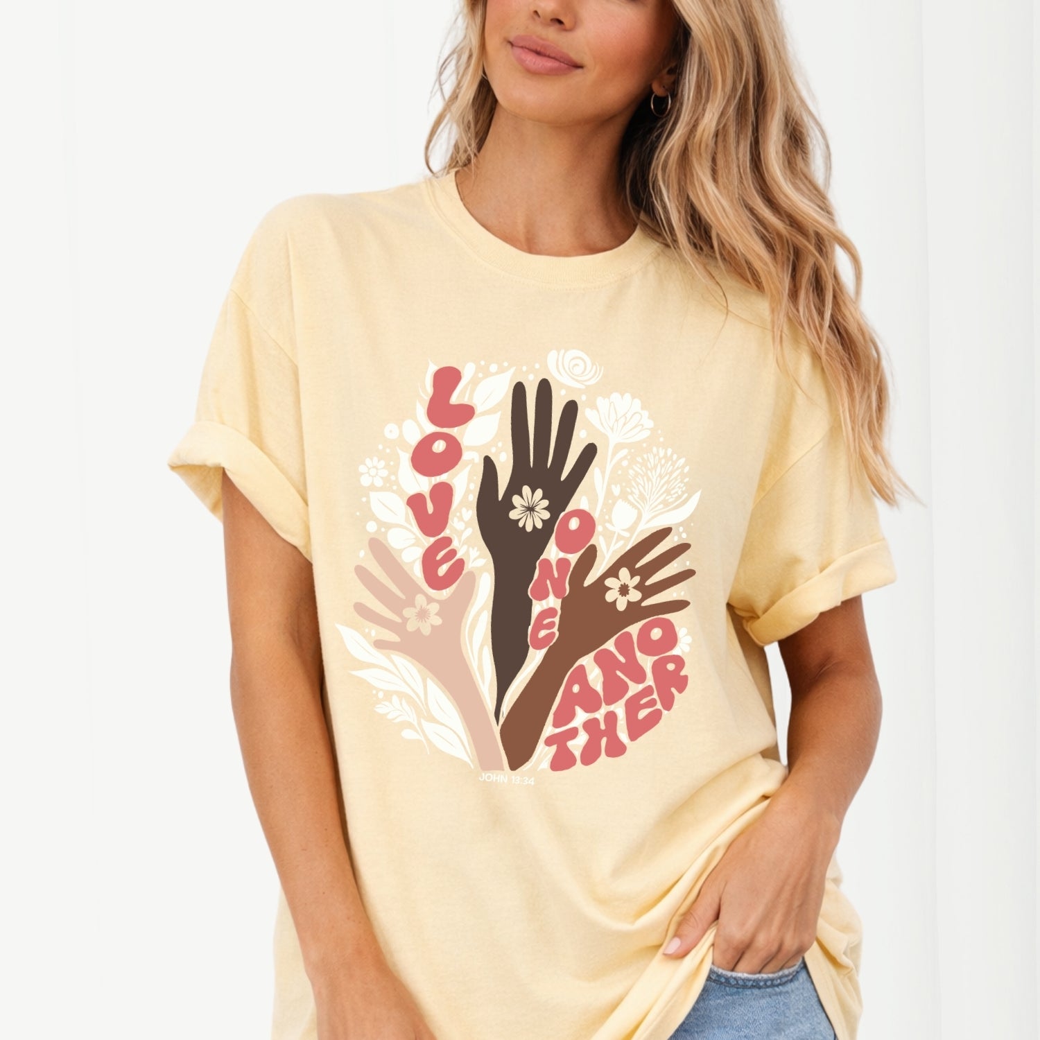 Woman wearing a yellow t-shirt with a graphic design of hands and text on a white background. John 13 Love One Another Comfort Colors Graphic Tee 