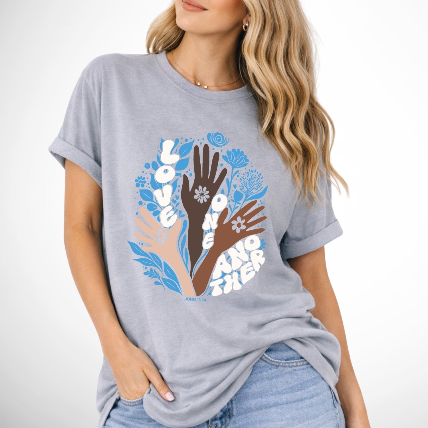 Person wearing a gray t-shirt with a colorful graphic of hands and flowers on a white background. John 13 Love One Another Comfort Colors Graphic Tee 