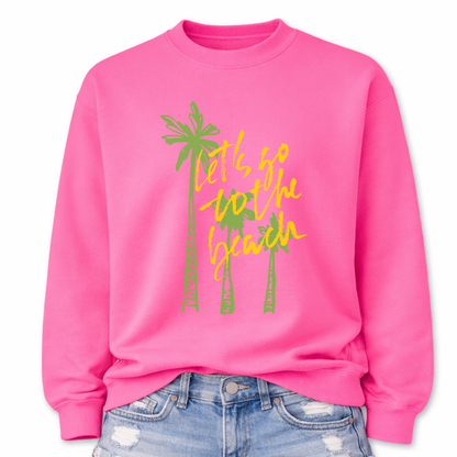 Tropical beach graphic on a classic pink crewneck sweatshirt. The design features three tall palm trees with the phrase Lets Go To The Beach layered across the center in a bold script style. The vertical palm tree layout creates a strong tropical silhouette that immediately communicates beach vacation style.