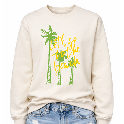 Tropical beach graphic on a classic off white crewneck sweatshirt. The design features three tall palm trees with the phrase Lets Go To The Beach layered across the center in a bold script style. The vertical palm tree layout creates a strong tropical silhouette that immediately communicates beach vacation style.