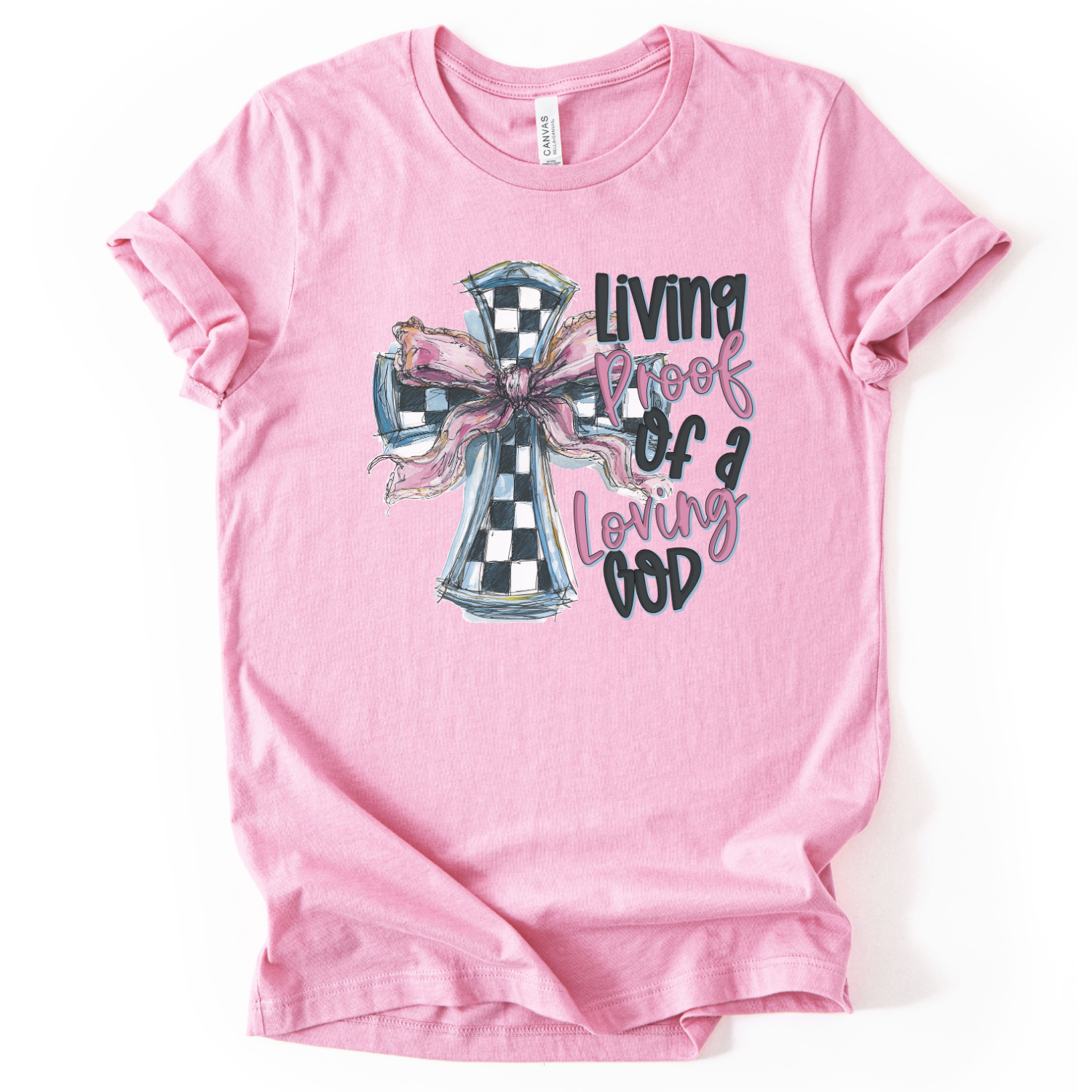 The graphic features an illustrated cross filled with a black-and-white check pattern, accented by a soft pink bow tied across the center. To the side, the phrase “Living Proof of a Loving God” appears in a mix of playful script and bold lettering.  On a pink Bella Canvas unisex t-shirt