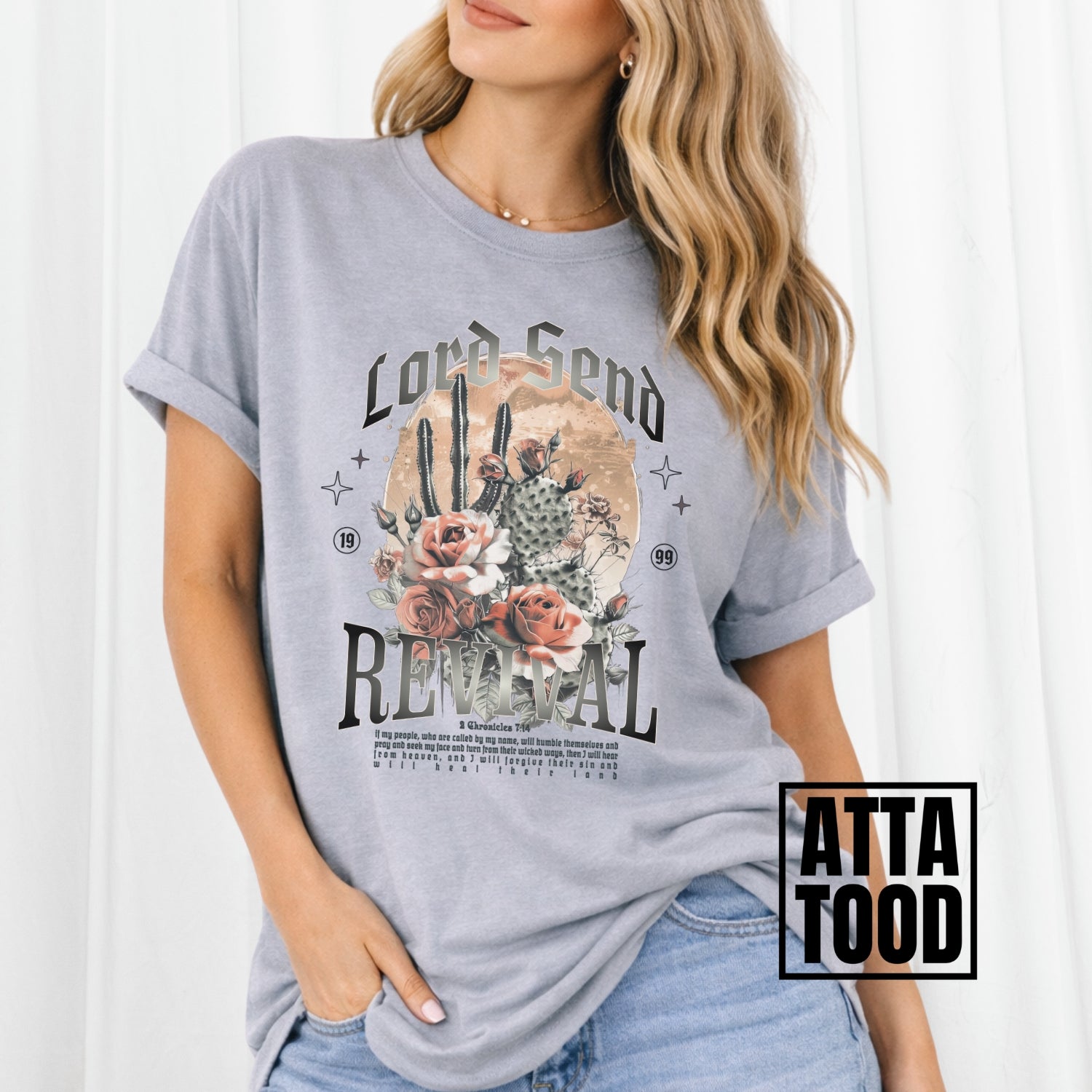 Woman wearing a gray t-shirt with a graphic design and text, standing against a white background. Lord Send revival featuring blooming cactuses