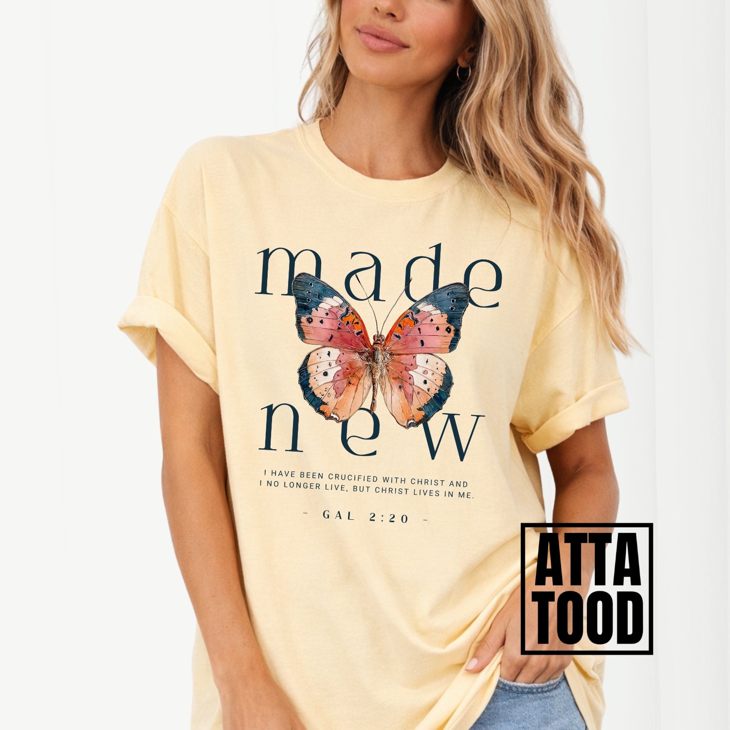 Woman wearing a yellow t-shirt with a butterfly graphic and text, brand 'Atta Tood' visible. Made new Galatians 2:20