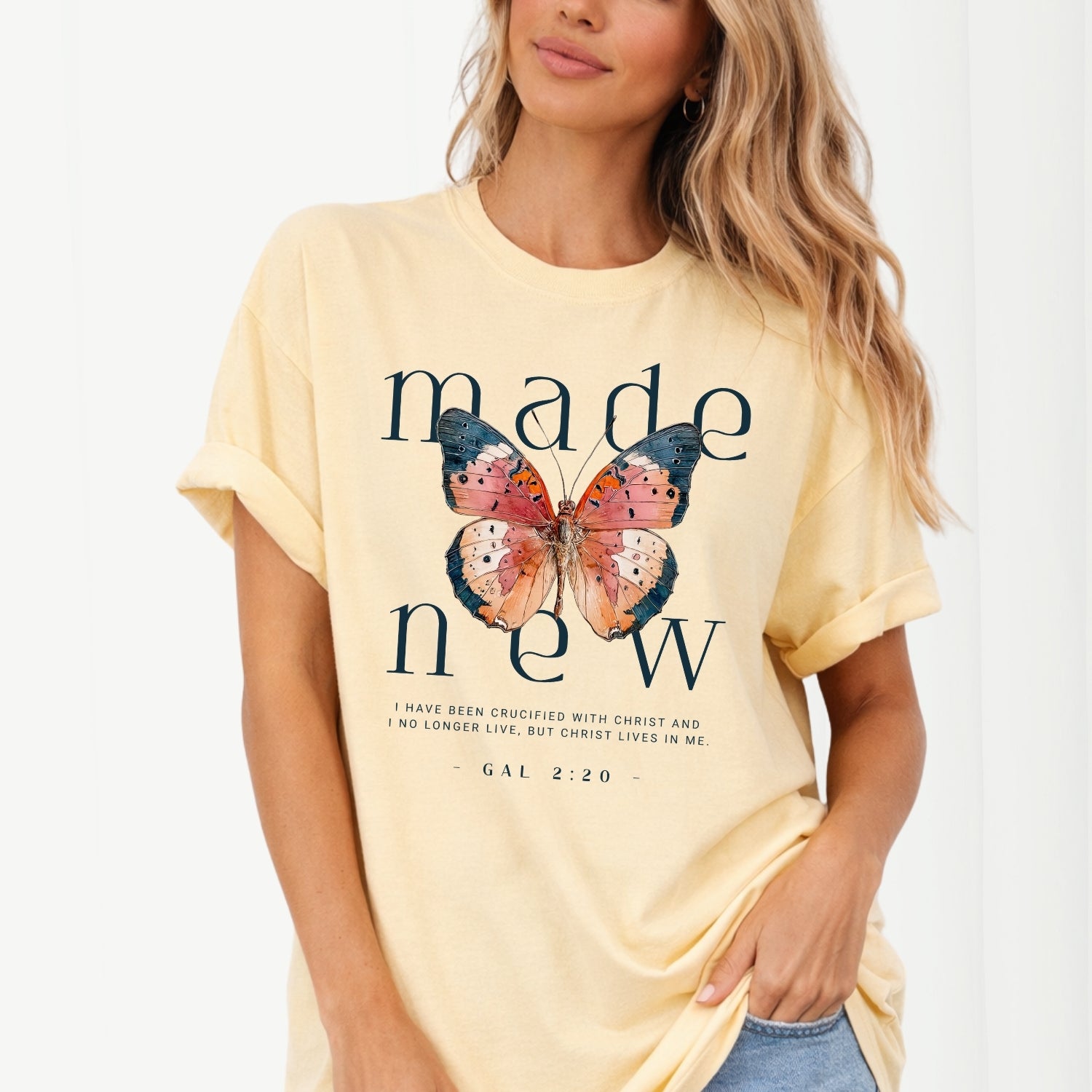 Woman wearing a yellow t-shirt with a butterfly graphic and text on a white background. Made New Bible Verse Comfort Colors Butterfly Graphic Tee