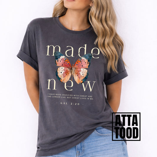 Woman wearing a dark gray t-shirt with a butterfly graphic and text, brand 'Atta Tood' visible. Made new Galatians 2:20